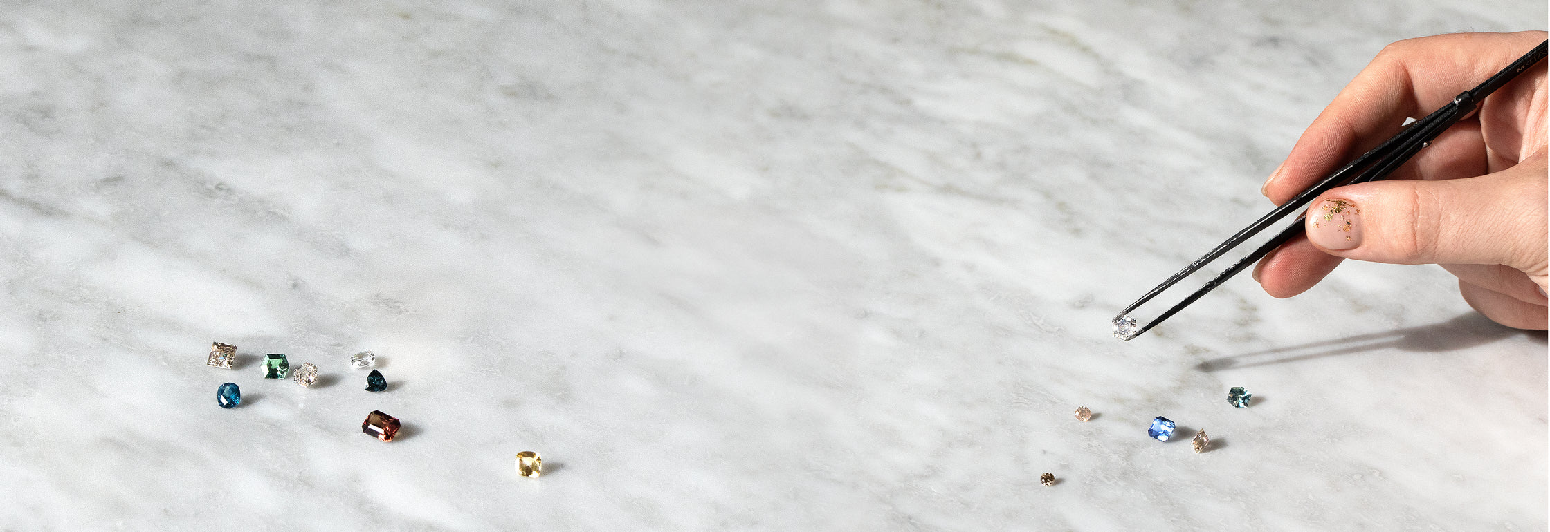 Hand with tweezers picking up gemstones on a marble background