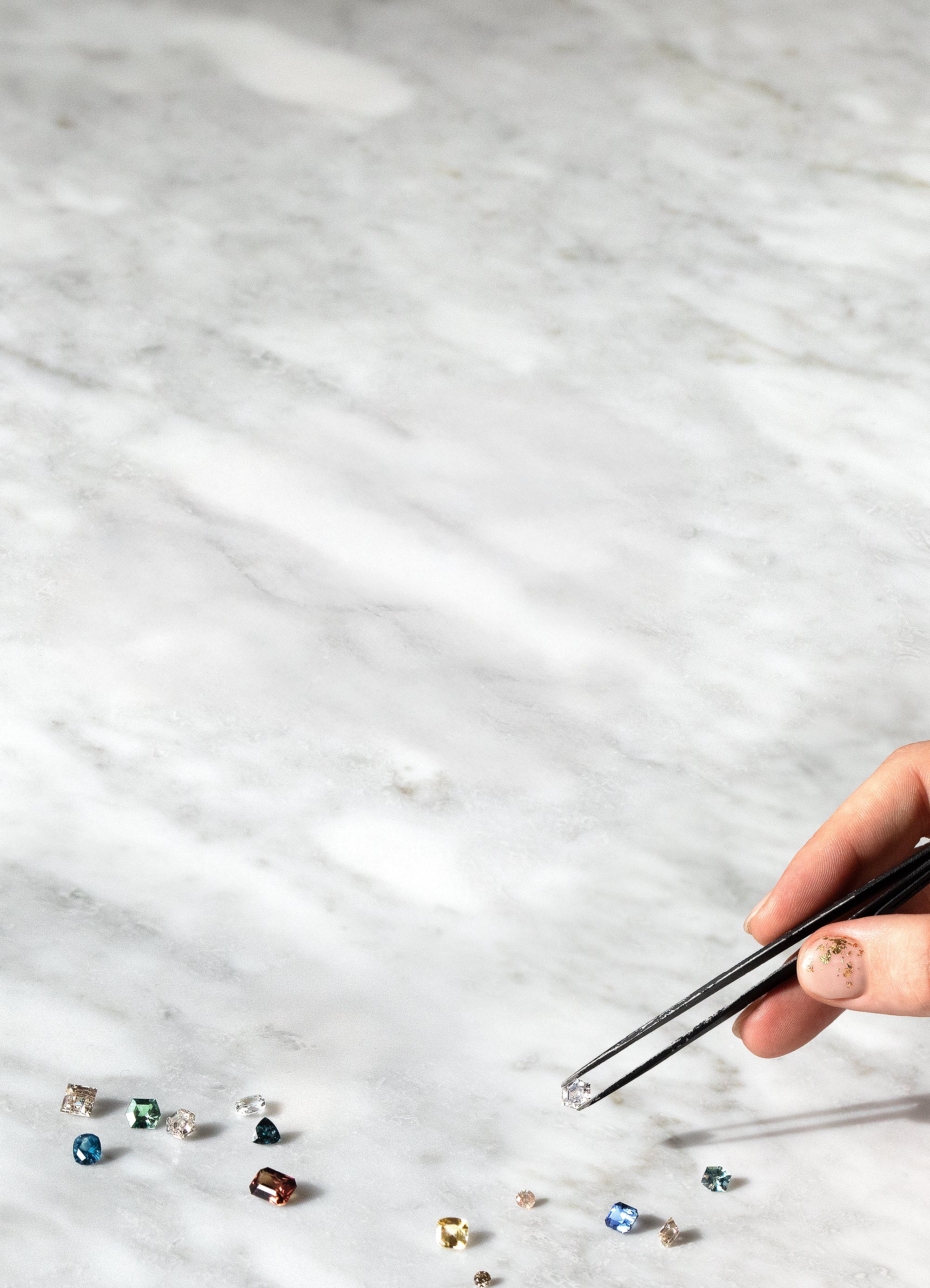 Hand with tweezers picking up gemstones on a marble background