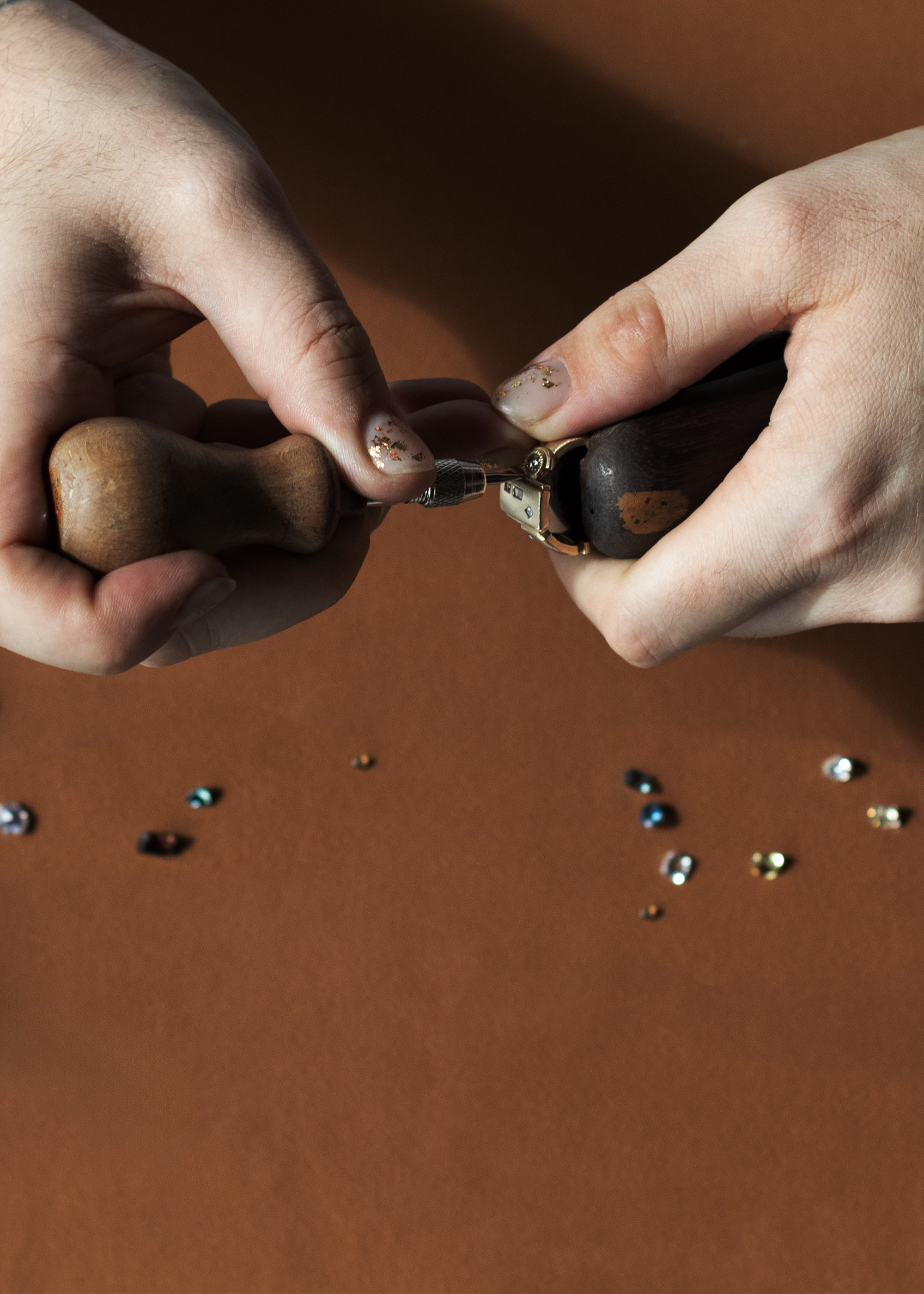 Hands setting a stone in a gold ring on a brown background with gemstones