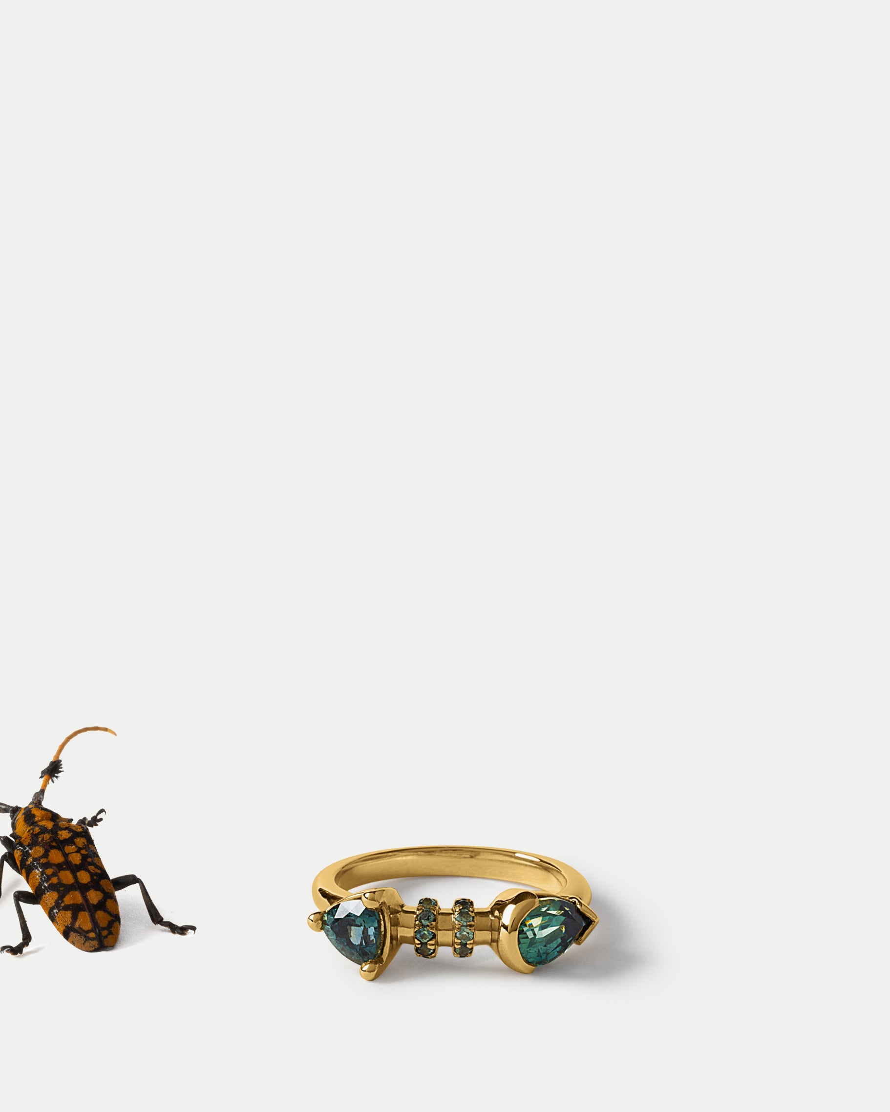 Angled view of Calabash Ring ft. Teal Sapphires in 14k yellow gold with an insect