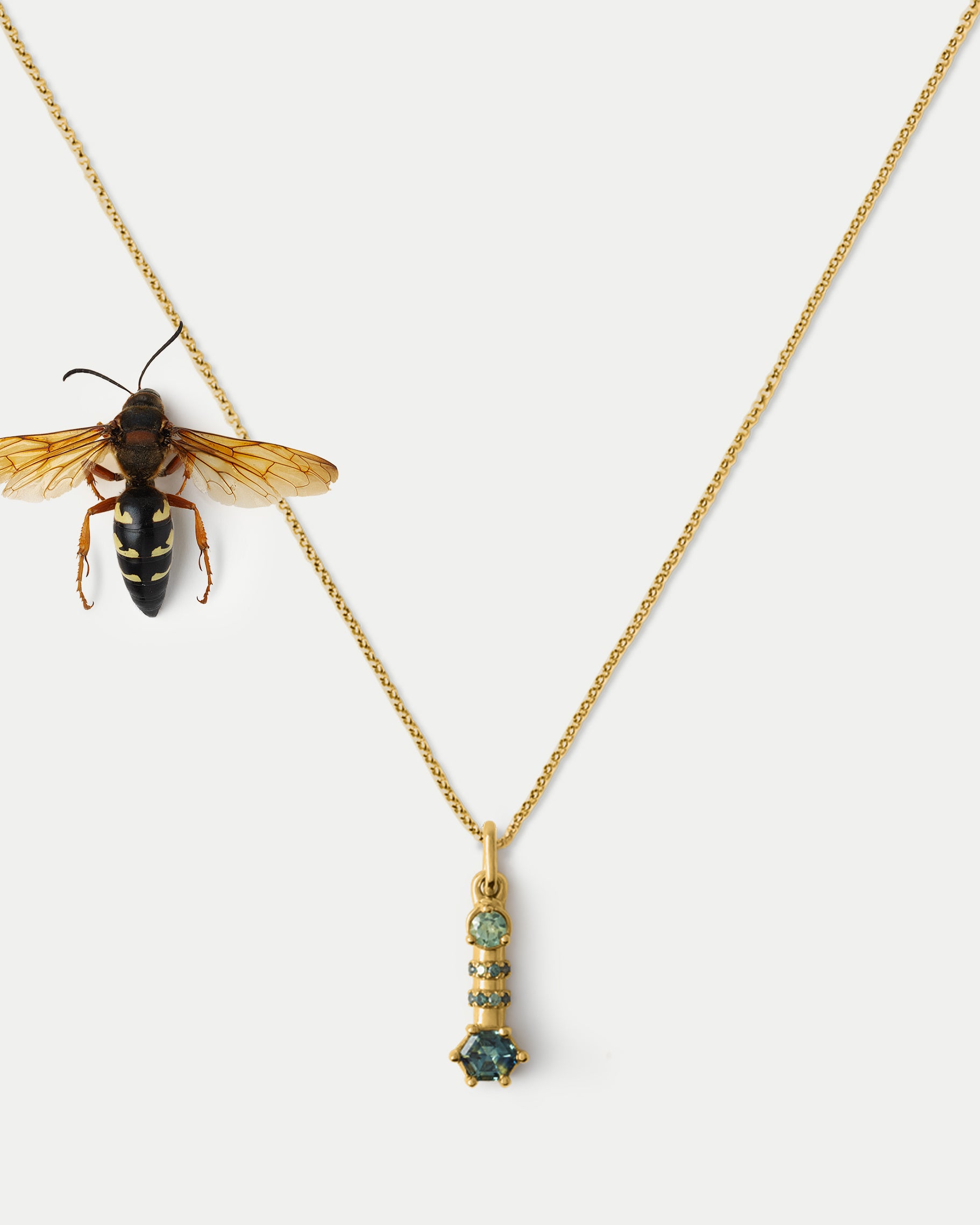 Clse up view of Monoceros Totem ft. Teal Sapphire in 14k yellow gold with an insect