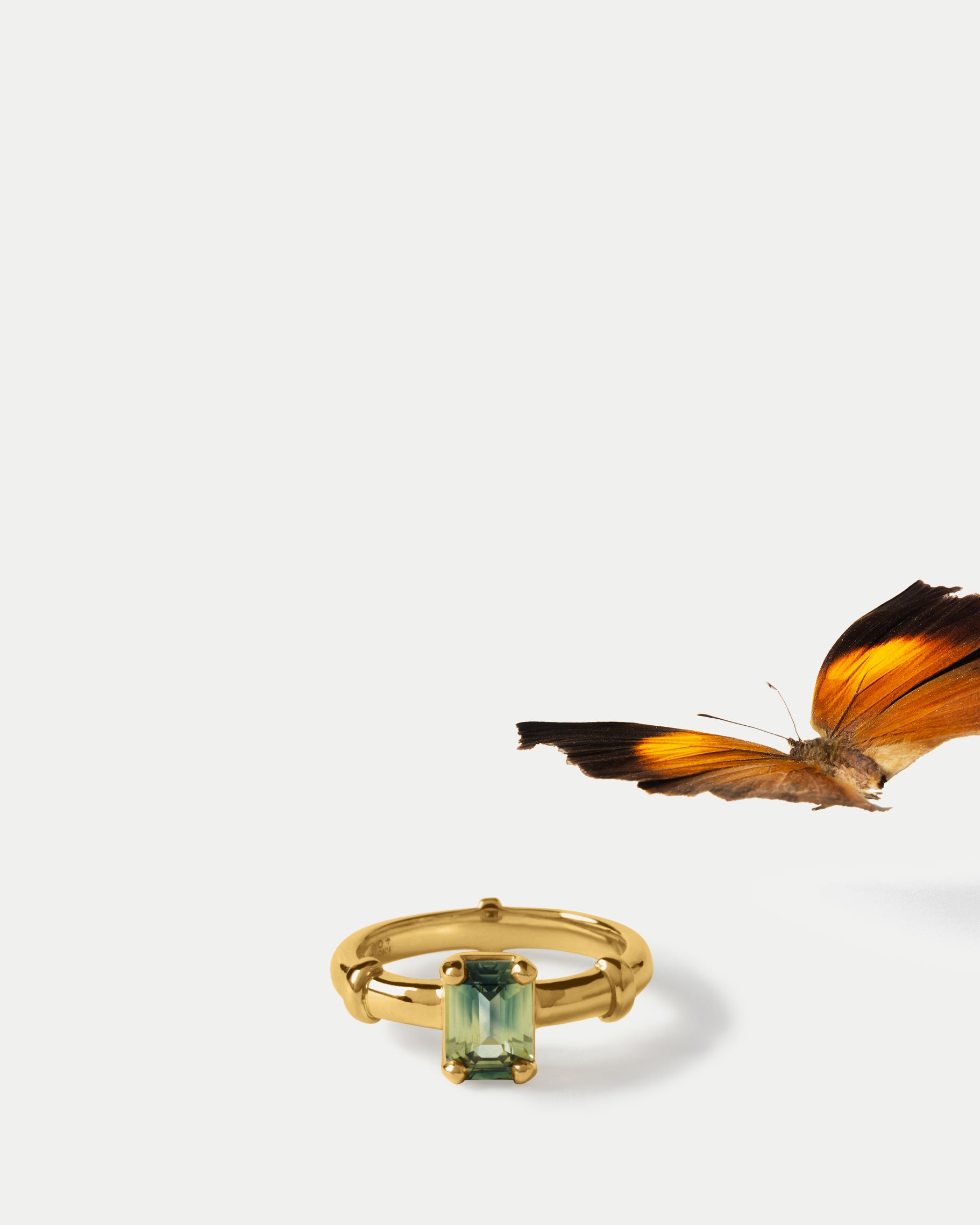 Angled view of Orion Solitaire Ring ft. Emerald Green Sapphire in 14k yellow gold with a butterfly